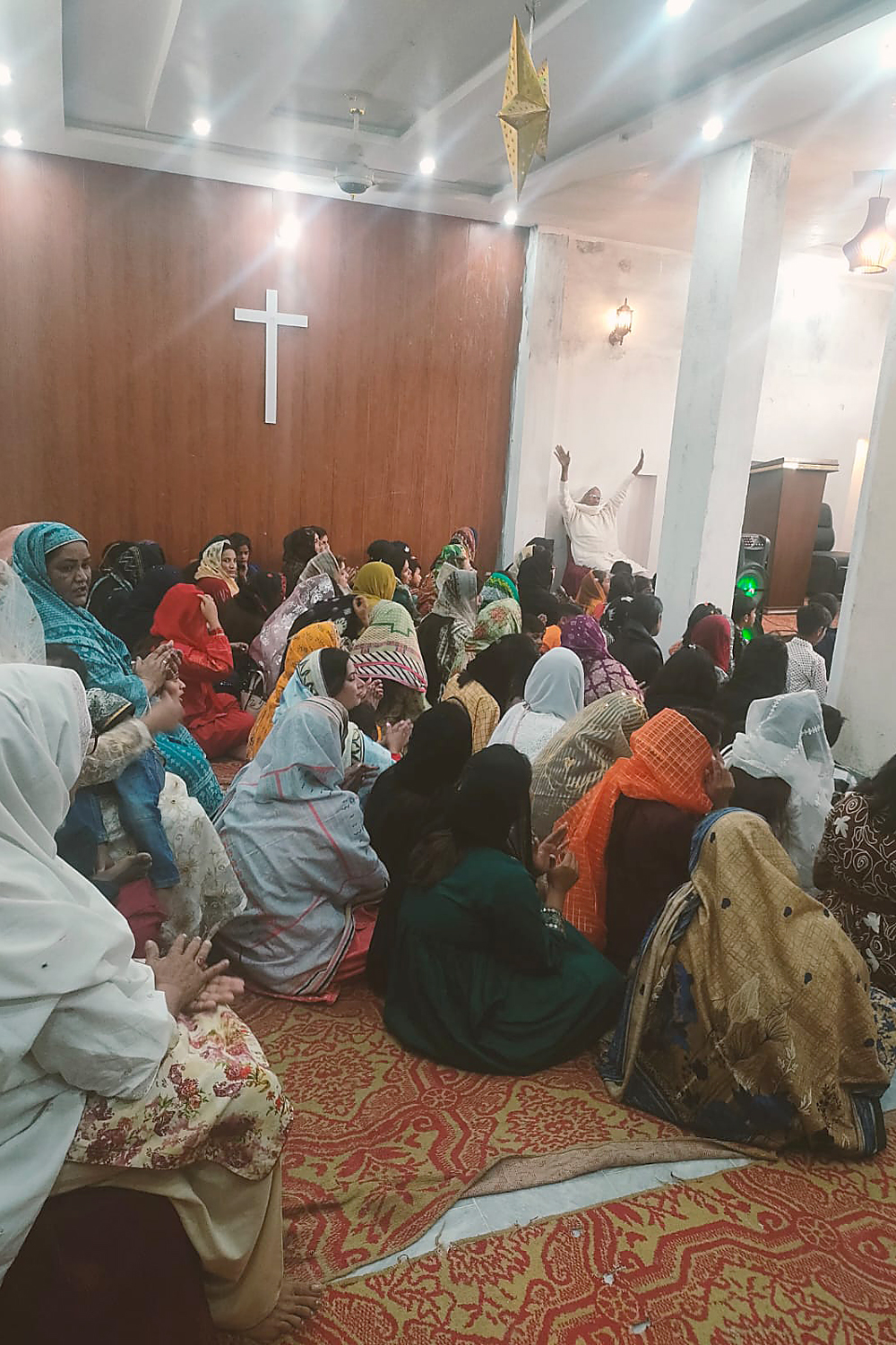 Traditionell gekleidete christliche Pakistani sitzen auf einem Teppich am Boden.