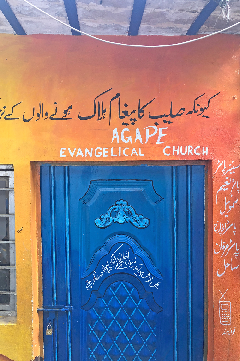 Orange Mauer und eine blaue Tür. Rund um die Tür arabische Schriftzeichen und die Worte AGAPE Evangelical Church