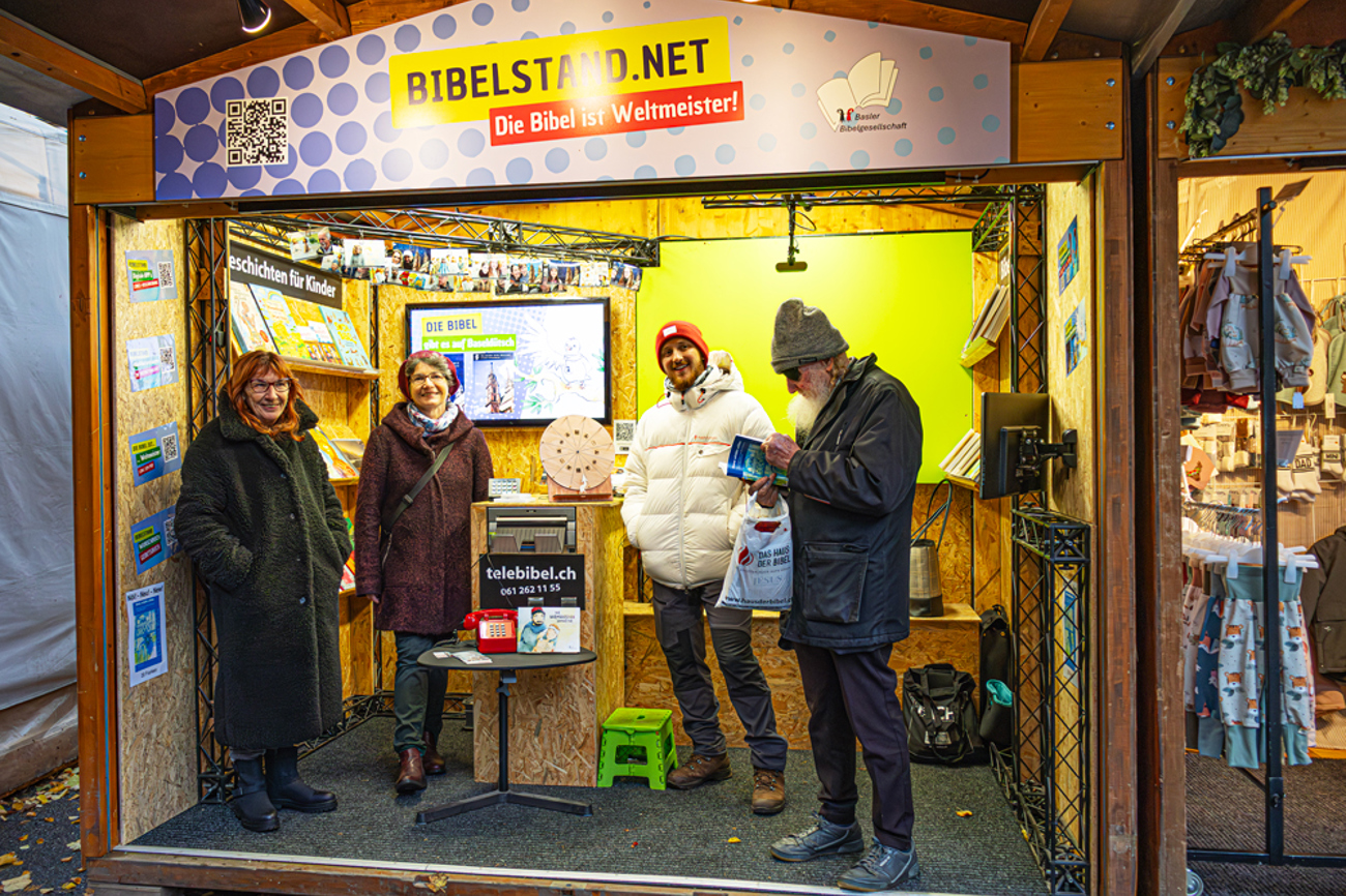 Mehr als nur ein Messestand: Der Bibelstand auf dem Petersplatz lädt zum Verweilen ein. Pfarrerin Mirjam Wagner, Sonja Weber und Timon Kuhn (v. l.) bilden an diesem Abend das Team. Ein Besucher blättert in einer Bibel. | Foto: Nicole Noelle