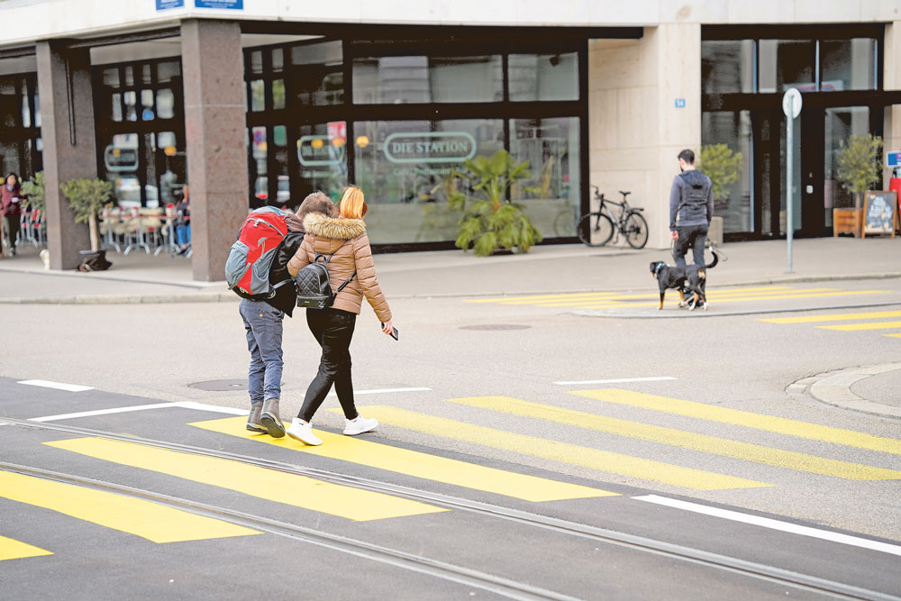Eine junge Frau hilft einem Menschen mit Einschränkungen über die Strasse.
